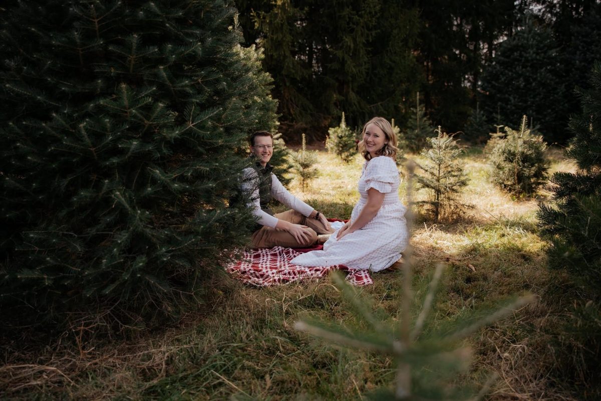 Max and Caitlin Wuethrich sitting on a picnic blanket among young evergreen trees